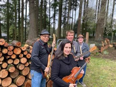 Three men, one woman with musical instruments in front of woodpile