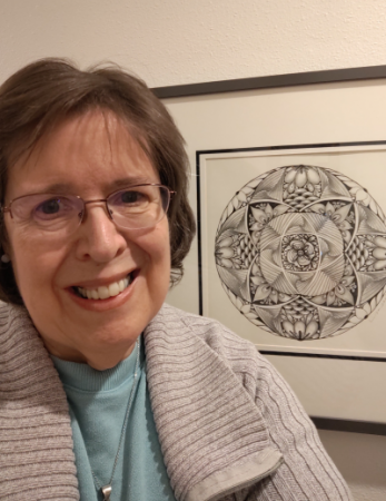 women with glasses in front of framed mandala artwork